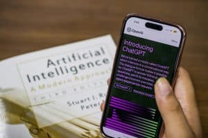 So start up Close-up of a smartphone displaying ChatGPT app held over AI textbook.