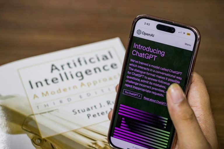 So start up Close-up of a smartphone displaying ChatGPT app held over AI textbook.